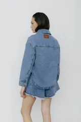 Campera de jean clásica con cierre frontal de botones metálicos, cuello camisero, bolsillos frontales con solapa y mangas largas con puños abotonados.