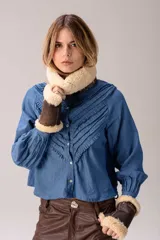 Camisa de denim azul con cuello mao y múltiples filas de volados en forma de V en el frente. Tiene mangas largas abullonadas con puños ajustados y cierre frontal de botones.