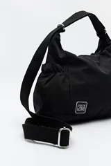 Cartera tipo hobo de nylon color negro, con diseño soft, correa regulable y parche con logo de la marca Piece of Cake.