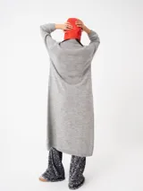 Buzo largo gris de tejido de punto grueso con cuello alto y capucha con orejas de conejo rojas. Tiene mangas largas y un tajo lateral.