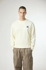 Buzo de cuello redondo en color crema, confeccionado en algodón, con detalle de logo en forma de cruz bordado en el pecho.