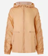 Campera deportiva femenina tipo parka, color ocre, confeccionada en poliamida y poliéster. Tiene cuello con capucha, mangas largas con puños elásticos, cierre frontal con cremallera y cordón ajustable en la cintura.