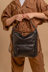 Cartera mochila de cuero sintético color negro, con diseño versátil que permite usarla como mochila o al hombro. Cuenta con un compartimento principal amplio y bolsillos frontales con cierre metálico.