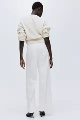 Pantalón de jean blanco de tiro alto, pierna ancha y corte holgado. Presenta bolsillos parche delanteros y traseros, y un detalle de ribete trenzado decorativo en la cintura.