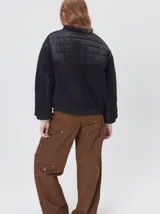 Campera crop de corte boxy y color negro, forrada en corderito, con parches capitoneados en el pecho y las mangas. Cuenta con cierre frontal metálico, cuello alto, puños y bajo elastizados, y detalle de logo bordado en hilo en el pecho.