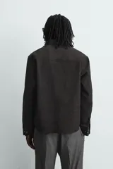 Sobrecamisa de corte relajado confeccionada en tejido efecto piel color marrón oscuro. Presenta cuello solapa, cierre frontal con botones metálicos, mangas largas con puños abotonados y dos bolsillos de plastrón con solapa en el pecho.