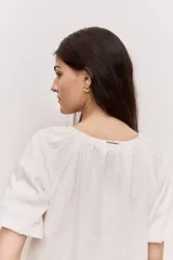 Blusa blanca de manga corta, con escote redondo y cierre frontal con tres botones. Presenta pliegues frontales y diseño liviano.