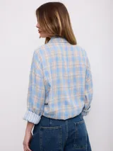 Camisa oversize de manga larga con estampado a cuadros en tonos rosado, amarillo y blanco, cuello camisero y cierre frontal con botones.