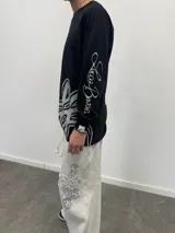 Remera manga larga de algodón color negro, con diseño gráfico abstracto en tono gris en la parte inferior frontal y tipografía cursiva en la manga. Presenta cuello redondo reforzado y grifa de la marca en el puño.