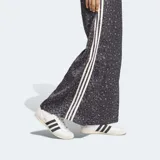 Pantalón Adidas Originals wide leg de satén, con estampado animal print en tonos grises y negros, cintura elástica y las clásicas tres tiras blancas a lo largo de los laterales.