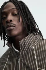 Cazadora de corte boxy fit confeccionada en tejido técnico. Presenta un diseño a rayas verticales, cuello subido, cierre frontal de cremallera y mangas largas con puños elásticos. Incluye bolsillos laterales con cremallera oculta y detalles de paneles en contraste.