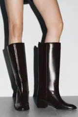 Bota alta de caña media en color marrón oscuro, con diseño minimalista, punta redonda y tacón bloque de madera. Cuenta con tirador trasero para facilitar el calce.