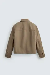 Sobrecamisa de corte boxy fit confeccionada en algodón con estructura canvas y efecto lavado. Presenta cuello solapa, cierre frontal con botones, mangas largas con puños abotonados y bolsillos de plastrón con solapa en el pecho. Incluye detalles bordados a tono en las mangas.