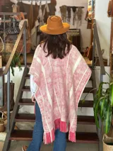 Ruana de lana merino tejida en telar, con diseño de rayas verticales en tonos crudo y rojizo, y terminación de flecos en el ruedo.