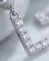 Par de aros de acero quirúrgico tipo argolla con dije colgante en forma de letra con incrustaciones de circonitas.