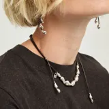 Gargantilla de cuero marrón oscuro con dijes metálicos plateados en forma de gota y cierre de mosquetón con cadena de alargue.