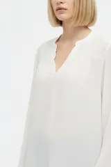 Blusa blanca de viscosa con detalles de broderie en los hombros, cuello en V y mangas largas holgadas.