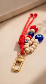 Cartera tipo hobo de cuero sintético color suela, con interior espacioso y costuras decorativas frontales. Incluye asa de hombro fija, monedero rectangular colgante a juego y un llavero amuleto con cuentas de madera, ojos turcos y detalles en rojo.