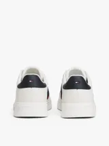 Zapatillas urbanas Tommy Hilfiger de corte bajo, confeccionadas en piel lisa color blanco. Presentan paneles laterales en azul marino y rojo, cordones oscuros y suela de goma gruesa con diseño dentado. Incluyen detalles de la marca en la lengüeta, lateral y talón.