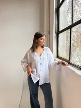 Camisa blanca de lino, con cuello en V, cierre frontal de botones y mangas amplias de corte holgado.