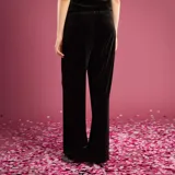 Pantalón de corte ancho y fluido confeccionado en terciopelo negro, con cintura de tiro medio y cierre frontal.
