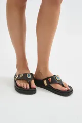 Ojotas de dedo negras con suela plana y gruesa, decoradas con apliques metálicos de piedras de colores en la tira.