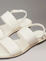 Sandalias planas blancas de cuero sintético, con puntera cuadrada y dos tiras anchas. La tira superior tiene el logo de Calvin Klein grabado.
