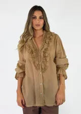 Blusa de algodón color tostado, de manga larga con puños fruncidos y cierre frontal con botones. Presenta volados decorativos con detalles de encaje alrededor del escote en V.