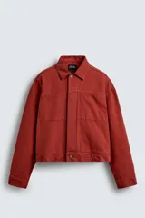 Cazadora de algodón color terracota, de corte cropped y calce holgado. Presenta cuello solapa, manga larga con puño abotonado, dos bolsillos de vivo en el pecho y bolsillos laterales en la cadera. Cierre frontal con botonadura oculta.