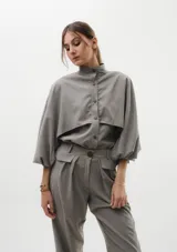 Camisa de seda peletizada con diseño de capa integrada, cuello mao y mangas abullonadas. Presenta cierre frontal con botones al tono y una estructura unida en cuello, puños y cartera.
