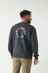 Buzo de felpa color beige con cuello redondo, manga larga y puños acanalados. Presenta un logo circular estampado en el frente.