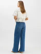Camisa de algodón blanca con cuello clásico y cierre frontal de botones. Presenta un diseño con capas superpuestas y volados, combinando paneles de tela lisa con tejido bordado suizo de motivos calados y una cenefa decorativa. Posee mangas cortas y una silueta acampanada.