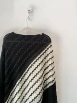 Poncho de tejido abierto en color negro con una franja diagonal en color blanco, con patrón geométrico texturizado.