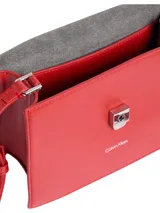Cartera de mano estructurada color rojo, con asa superior tubular y correa ajustable para cruzar. Presenta cierre desplegable con pulsador y logo metálico grabado de Calvin Klein en el frente.