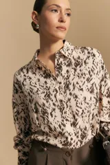 Camisa de manga larga con cuello camisero y cierre frontal de botones. Presenta un diseño de silueta relajada y un estampado abstracto en tonos beige y marrón oscuro.