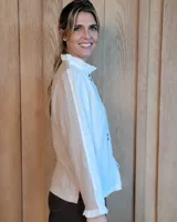 Camisa de manga larga con estampado de rayas verticales en tonos crudo y beige. Presenta cuello alto con volados, cierre frontal con botones dobles y puños con volados.