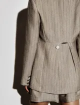 Blazer de corte sastrero en color beige con estampado de rayas verticales finas. Presenta solapas clásicas, cierre frontal con dos botones, bolsillos delanteros con solapa y botones decorativos.