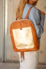 Mochila de cuero color tostado con bolsillo frontal dorado y cierre plateado.