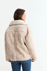 Chaqueta de simil gamuza en color beige, con forro interno y cuello de corderito sintético. Presenta un diseño de corte holgado, cierre frontal con botones y bolsillos laterales.