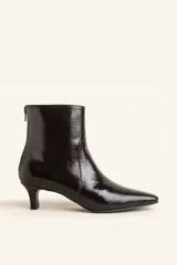 Bota corta de cuero vacuno con acabado brillante tipo charol, color negro. Presenta punta fina, cierre trasero y taco chupete bajo.