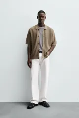 Camisa de punto de manga corta, color marrón topo, con cuello solapa y cierre frontal de botones. Presenta un tejido texturizado y un calce relajado.