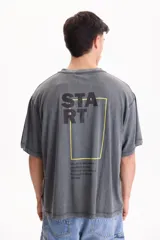 Remera gris de manga corta, corte oversize con efecto acid wash y estampa en la espalda con la palabra "START" y un marco amarillo.