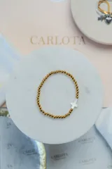 Pulsera de esferas doradas con dije central en forma de cruz de color blanco nacarado.