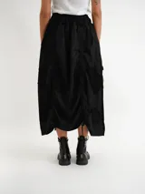 Pollera midi de diseño desestructurado en color negro, con cintura elastizada y detalles fruncidos con cordones ajustables a los lados.