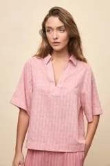 Blusa rosada de manga corta con cuello camisero y escote en V, confeccionada en tejido liviano con textura y diseño de pequeños lunares en relieve y finas rayas verticales, de calce relajado.