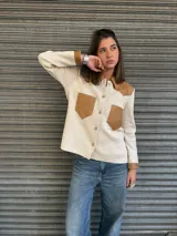 Camisa de tejido fino en lana color beige, con detalles en cuero color suela en cuello, bolsillos frontales y puños. Presenta cierre frontal con botones.