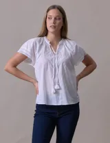 Blusa blanca de algodón marca Cupio, con cuello a la base, escote en V y lazo de ajuste. Presenta bordado en la parte delantera y mangas cortas amplias con aplique de puntilla.