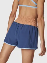 Short deportivo 2 en 1 de color azul con calza interior incorporada. Presenta una cintura ancha elástica en color tostado, ribetes en color celeste y bolsillos funcionales. Confeccionado con tecnología de secado rápido y materiales reciclados.