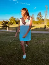 Vestido corto tejido en hilo de algodón color celeste, con cuello y espalda con apliques de cuero artesanal en tonos marrón, blanco y celeste.