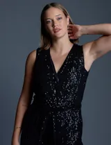 Enterito de lentejuelas marca Ninety, color negro, con escote en V cruzado y diseño sin mangas. Presenta cintura elastizada con lazo de ajuste, bolsillos frontales y abertura en la espalda con cierre invisible. Incluye forro interno a tono.